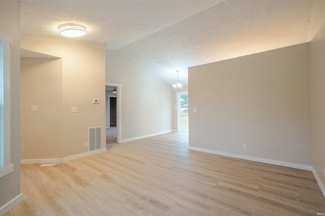 spare room with a textured ceiling, light wood-type flooring, an inviting chandelier, and vaulted ceiling