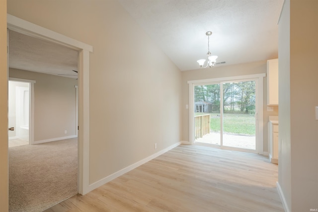 unfurnished dining area featuring a textured ceiling, light wood-type flooring, an inviting chandelier, and lofted ceiling