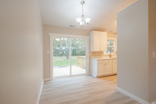 unfurnished dining area with a notable chandelier, sink, and light wood-type flooring