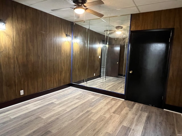 unfurnished room featuring wooden walls, light hardwood / wood-style flooring, ceiling fan, and a drop ceiling