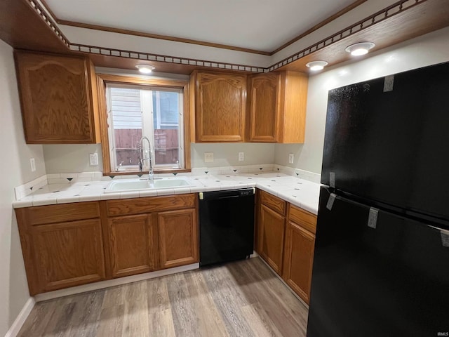 kitchen with black appliances, crown molding, sink, light hardwood / wood-style flooring, and tile counters