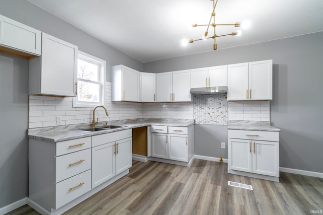 kitchen with hardwood / wood-style flooring, backsplash, white cabinetry, and sink