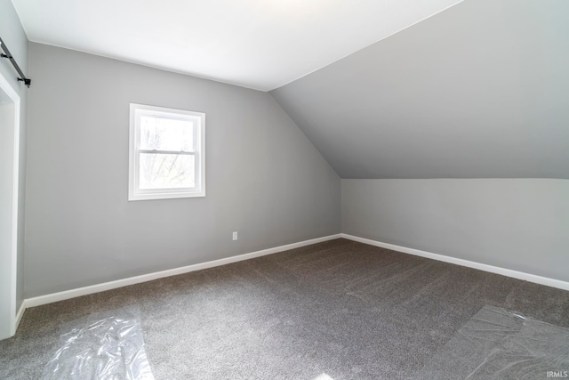 additional living space featuring carpet, a barn door, and vaulted ceiling