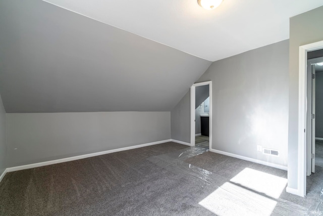 additional living space featuring dark colored carpet and lofted ceiling