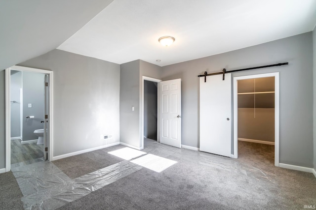 unfurnished bedroom with light carpet, ensuite bath, a barn door, a spacious closet, and a closet