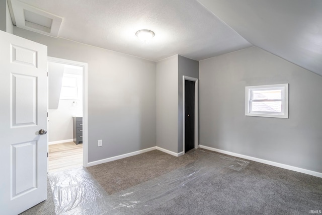 unfurnished bedroom featuring carpet flooring, a textured ceiling, and vaulted ceiling