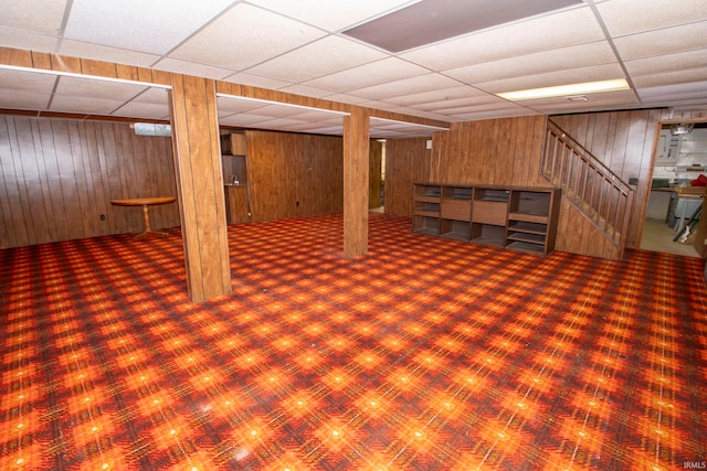 basement with a paneled ceiling and wood walls