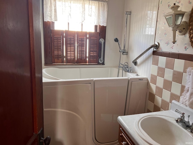 bathroom with vanity, tile walls, and a tub