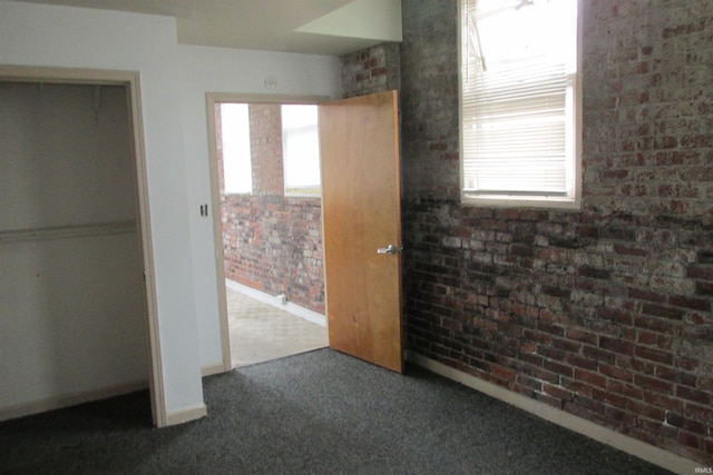 unfurnished bedroom with dark carpet, brick wall, and a closet