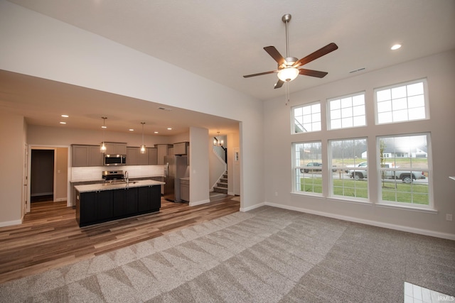 unfurnished living room featuring wood-type flooring, ceiling fan, a high ceiling, and sink