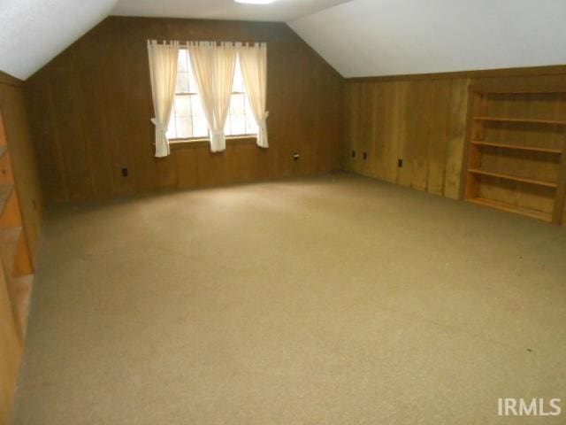 additional living space with wooden walls, light colored carpet, and lofted ceiling