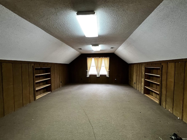 additional living space featuring lofted ceiling, wood walls, carpet, and a textured ceiling