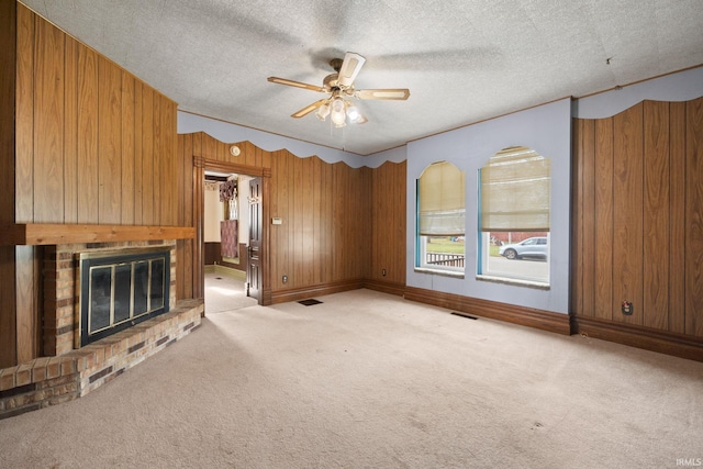 unfurnished living room featuring wood walls, a textured ceiling, light carpet, and a brick fireplace