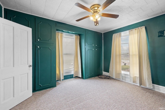 unfurnished bedroom with multiple windows, light colored carpet, and ceiling fan