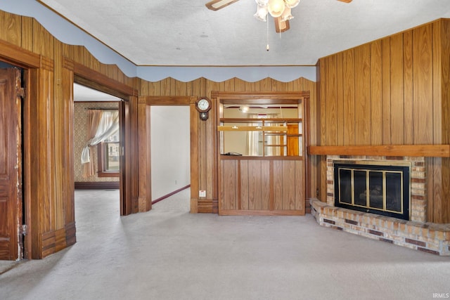 unfurnished living room with wooden walls, ceiling fan, a textured ceiling, and a brick fireplace