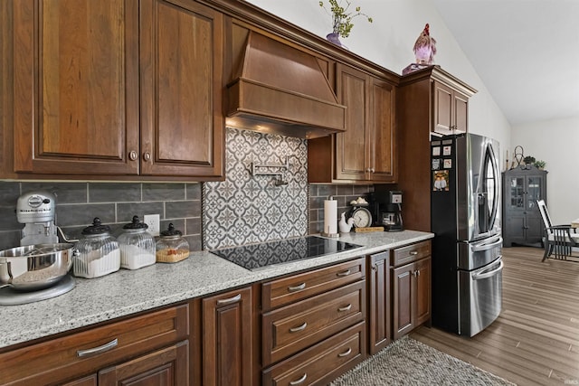 kitchen with black electric stovetop, light hardwood / wood-style flooring, custom range hood, tasteful backsplash, and stainless steel fridge with ice dispenser