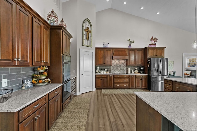 kitchen featuring backsplash, high vaulted ceiling, hanging light fixtures, light wood-type flooring, and appliances with stainless steel finishes