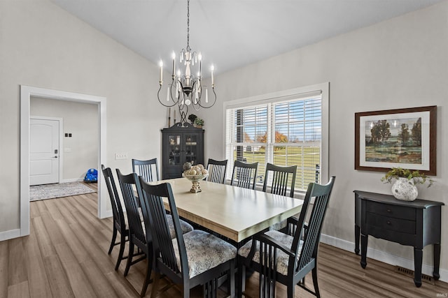 dining room with hardwood / wood-style flooring, vaulted ceiling, and a notable chandelier