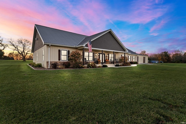 back house at dusk featuring a lawn and a porch