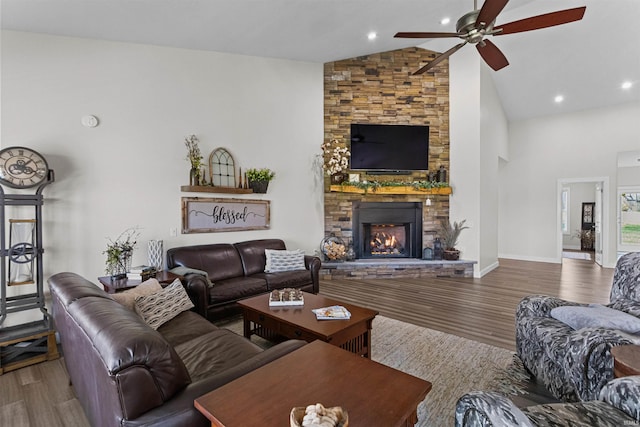 living room featuring wood-type flooring, high vaulted ceiling, a stone fireplace, and ceiling fan