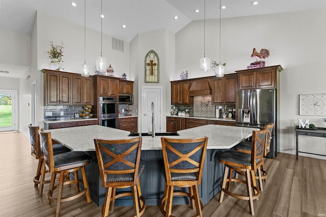 kitchen featuring backsplash, stainless steel appliances, a large island with sink, high vaulted ceiling, and hanging light fixtures