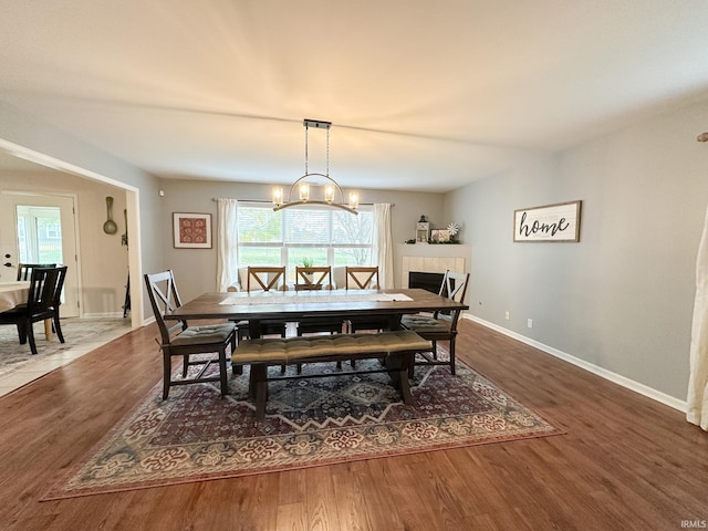 dining room featuring a tile fireplace, an inviting chandelier, baseboards, and wood finished floors