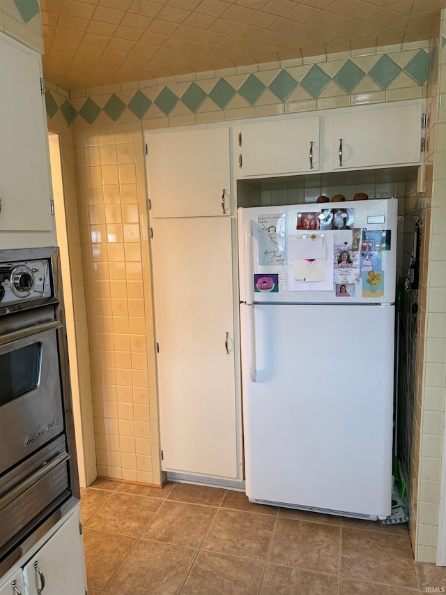 kitchen featuring black oven, white refrigerator, light tile patterned flooring, and white cabinetry