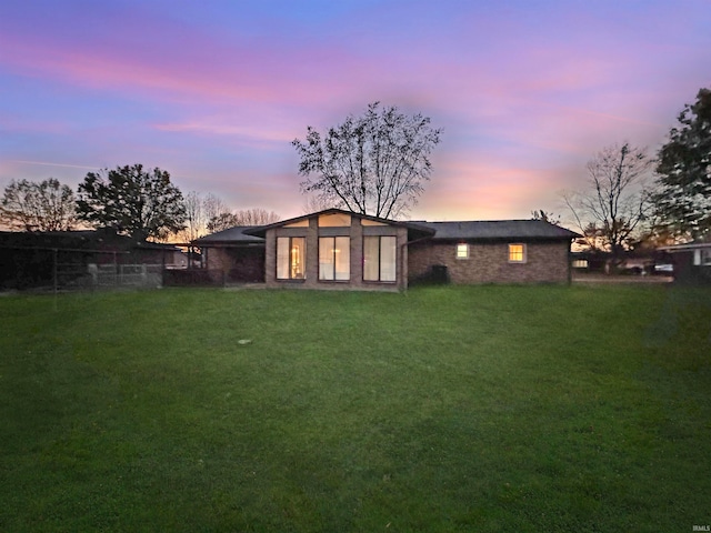 back house at dusk featuring a lawn