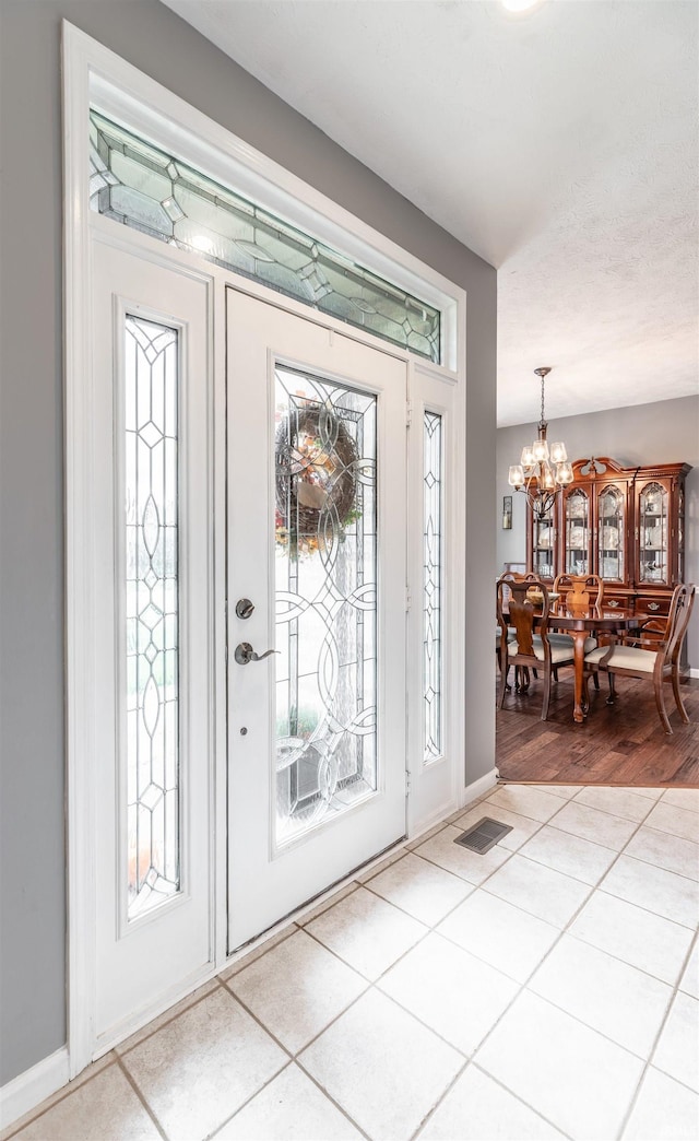 entryway with light hardwood / wood-style floors, a textured ceiling, and an inviting chandelier