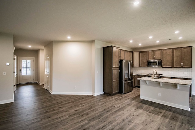 kitchen featuring backsplash, stainless steel appliances, sink, dark hardwood / wood-style floors, and an island with sink