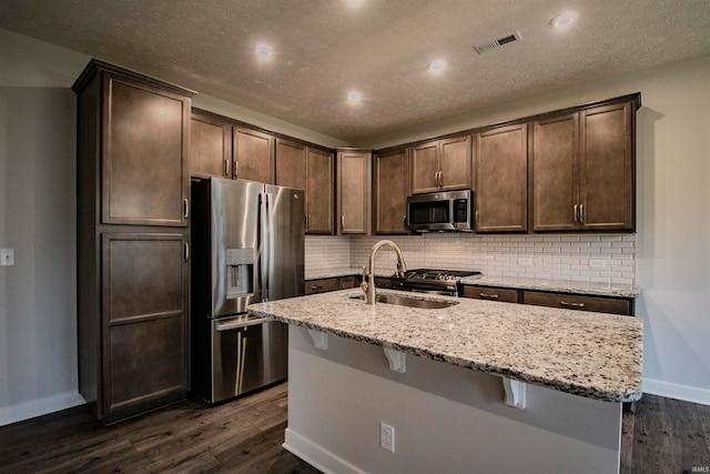 kitchen with sink, stainless steel appliances, an island with sink, and dark wood-type flooring