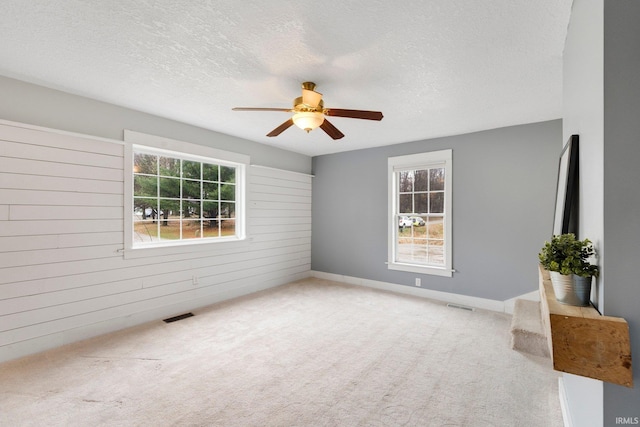 carpeted empty room with ceiling fan, wood walls, and a textured ceiling