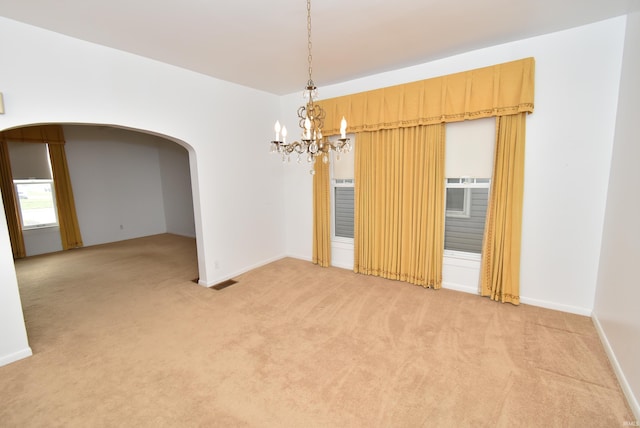 spare room featuring light carpet and a notable chandelier