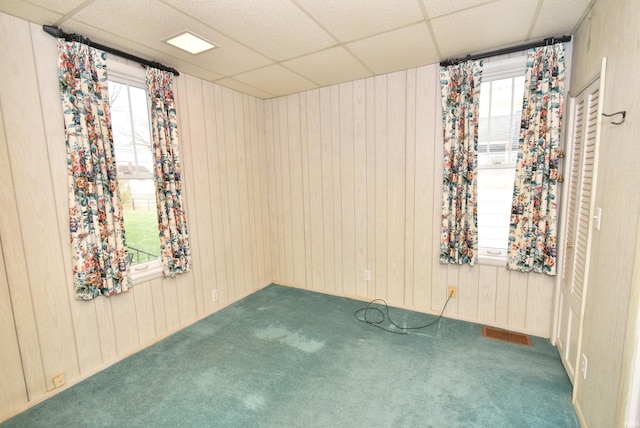 unfurnished room with wood walls, a drop ceiling, and carpet