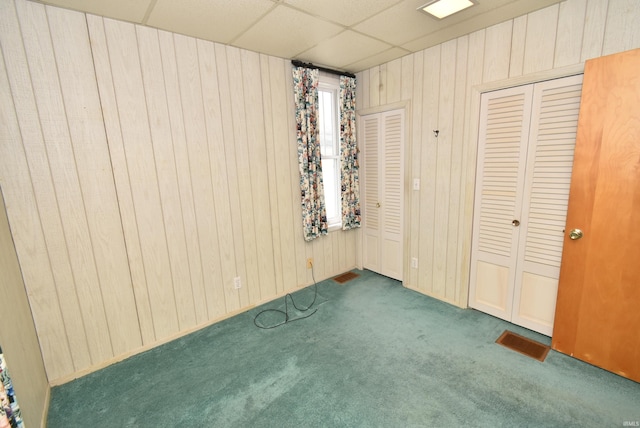 unfurnished bedroom with a paneled ceiling, wooden walls, and dark carpet