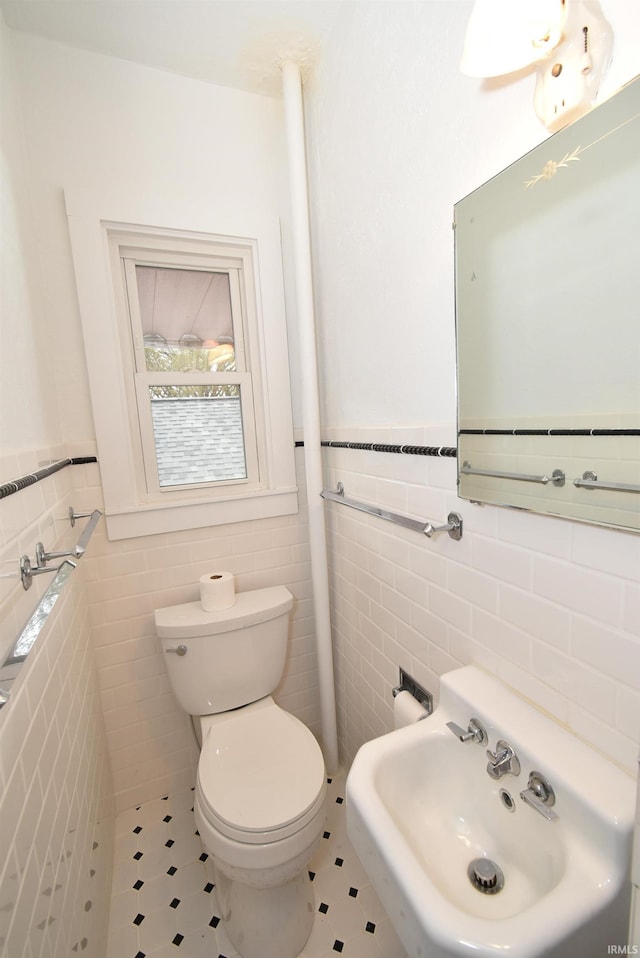 bathroom with toilet, sink, and tile walls