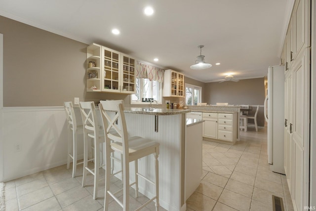 kitchen with crown molding, decorative light fixtures, white fridge, kitchen peninsula, and a breakfast bar area