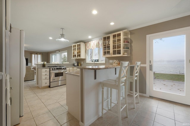 kitchen featuring high end range, a kitchen breakfast bar, a water view, light tile patterned flooring, and kitchen peninsula