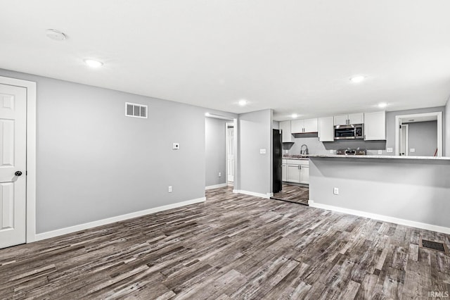 kitchen with sink, black fridge, dark hardwood / wood-style floors, kitchen peninsula, and white cabinets