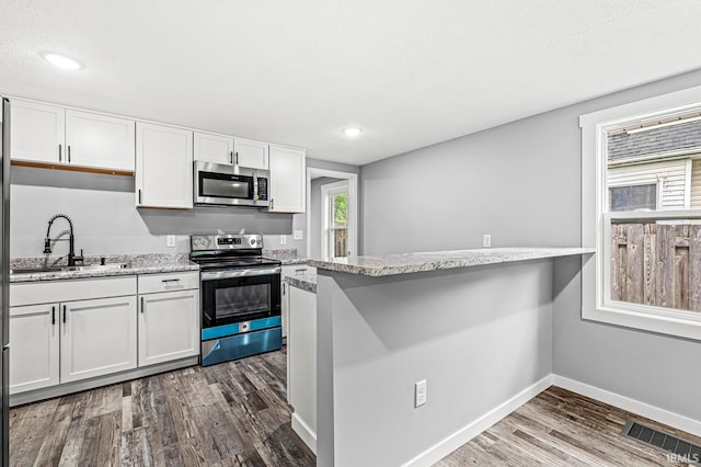 kitchen featuring white cabinets, stainless steel appliances, kitchen peninsula, and hardwood / wood-style flooring