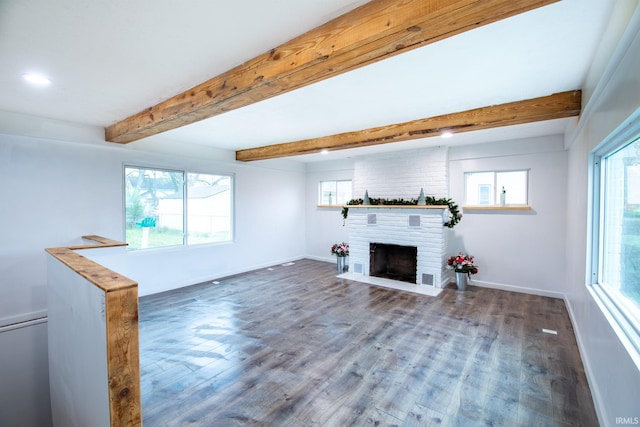 unfurnished living room featuring a healthy amount of sunlight, wood-type flooring, beam ceiling, and a brick fireplace