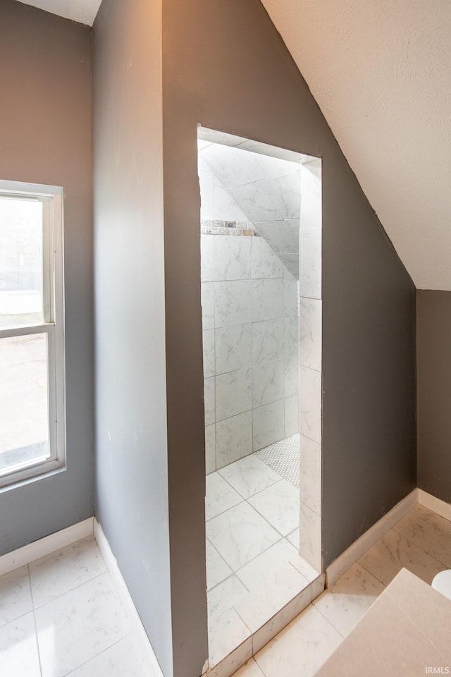 bathroom featuring tile patterned flooring, tiled shower, and vaulted ceiling