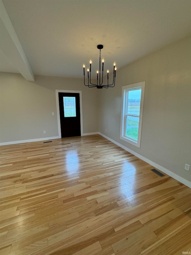 unfurnished dining area featuring light wood-type flooring, a healthy amount of sunlight, and a notable chandelier