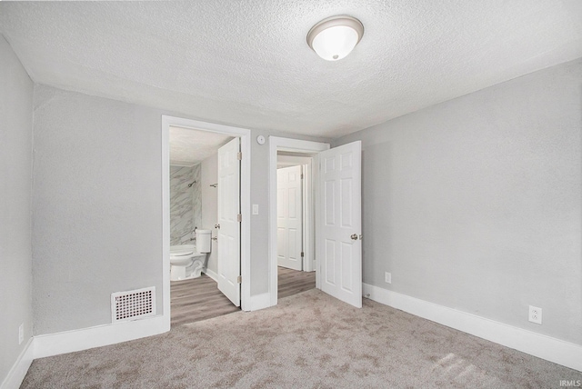 unfurnished bedroom with light colored carpet, a textured ceiling, and ensuite bath