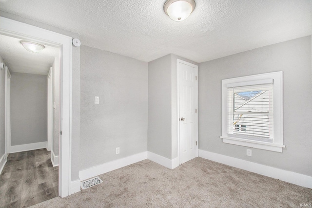 unfurnished room featuring a textured ceiling and light carpet