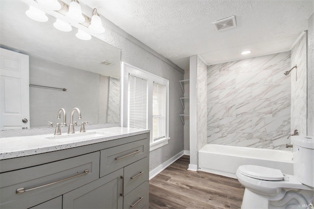 full bathroom with tiled shower / bath combo, wood-type flooring, a textured ceiling, toilet, and vanity