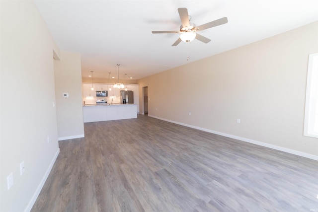 unfurnished living room featuring ceiling fan with notable chandelier, wood finished floors, and baseboards