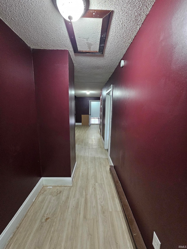 corridor with a textured ceiling and light hardwood / wood-style flooring