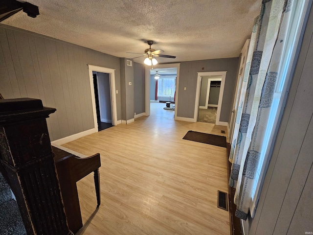 living room featuring wood walls, ceiling fan, light hardwood / wood-style floors, and a textured ceiling