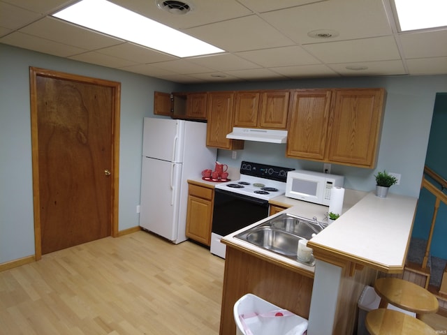 kitchen with white appliances, sink, light hardwood / wood-style flooring, kitchen peninsula, and a breakfast bar area